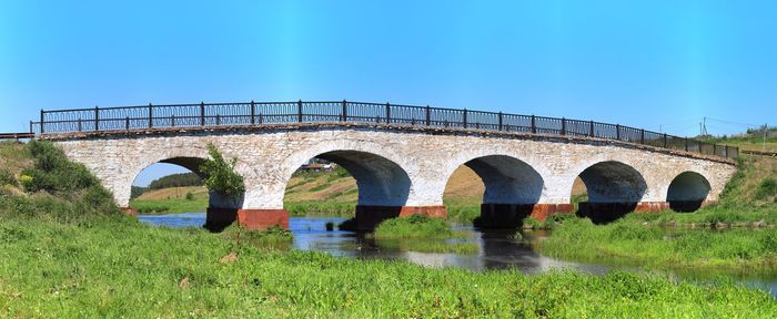 Arch bridge over river against clear blue sky