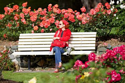Full length of woman looking away while sitting on bench at park