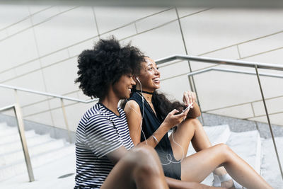 Two friends sitting on stairs listening music together with earphones and smartphone