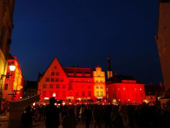 People on illuminated buildings in city against sky at night