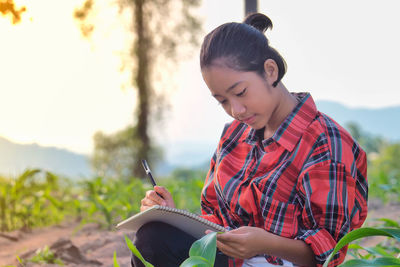 Girl writing in book while sitting on field