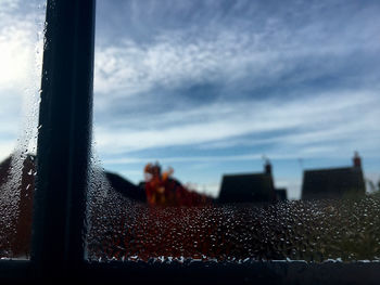 Close-up of wet glass window against sky