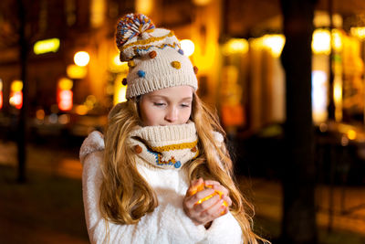 Night portrait of beautiful girl in knitted hat and scarf holding garland