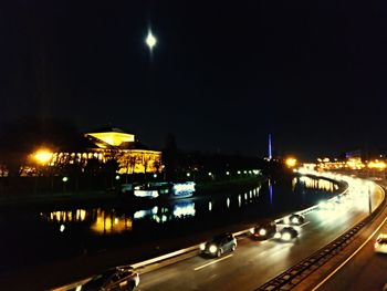 Illuminated city by river against sky at night