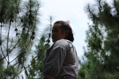 Portrait of young woman looking away against trees