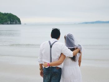 Rear view of couple standing at beach against sky