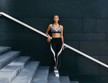 Portrait of young woman standing on staircase against wall