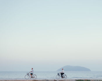 People riding bicycle at beach against clear sky