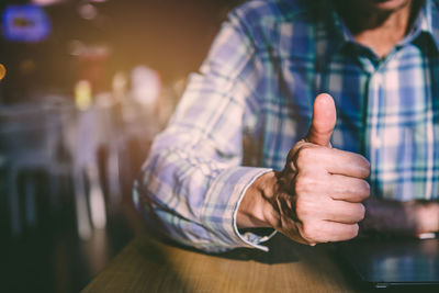 Midsection of man gesturing thumbs up while sitting at table