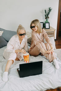 Blondes at home watch movie on laptop with 3d glasses and eat popcorn. concept of friendship