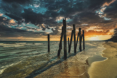 Wooden posts on beach against sky during sunset