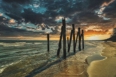 Wooden posts on beach against sky during sunset