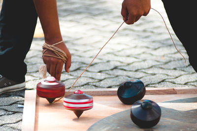 Low section of man playing with spinning top on wooden board over footpath