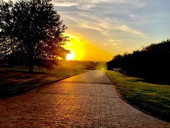 Road amidst trees against sky during sunset