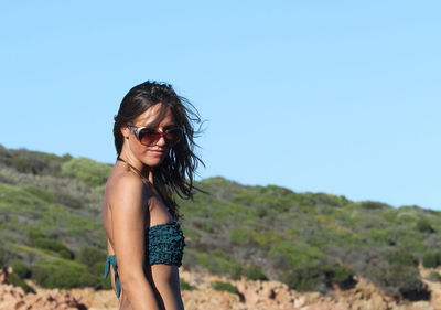 Young woman wearing sunglasses standing against clear sky