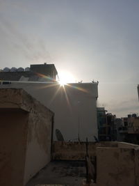 Sunlight streaming through buildings against sky during sunset