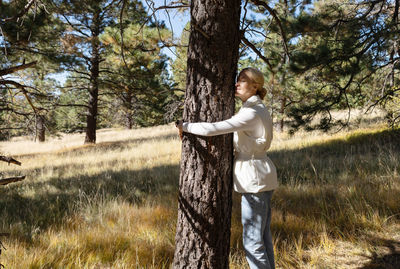 Blond woman in casual cloth hugs a tree in forest or park, enjoying its shadow. national love a tree