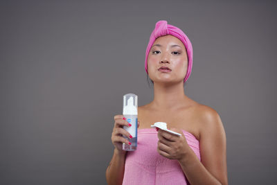 Portrait of smiling young woman holding bottle against gray background