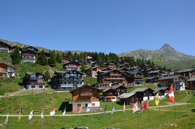 Houses on field by buildings against clear blue sky