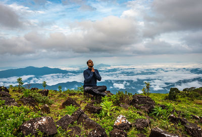 Man sitting on rock against sky