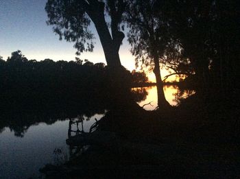 Silhouette trees by lake against sky during sunset