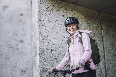 Portrait of senior woman with cycle standing near wall