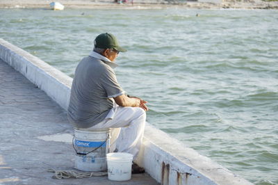 Rear view of man sitting on retaining wall by sea