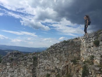 Low angle view of woman standing on cliff against cloudy sky