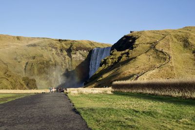 Panoramic view of road amidst land against clear sky with a warerfall in the background