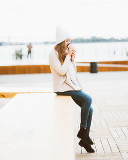 Side view of woman drinking coffee while sitting on retaining wall