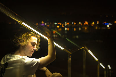 Young man by illuminated lights against sky at night