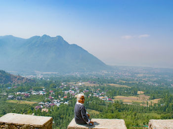Rear view of man sitting on mountain against sky