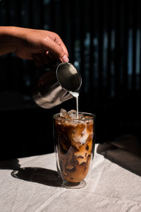 Close-up of hand pouring coffee in glass on table