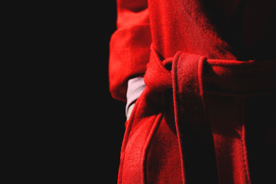 Midsection of person wearing red bathrobe against black background