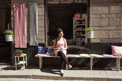 Thoughtful owner having coffee while sitting on table by cushions outside fabric shop