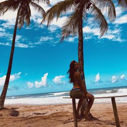 Full length woman posing under palm tree at beach against sky