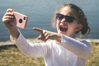 High angle view of happy girl taking selfie with mobile phone while standing against lake