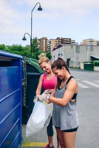 Young woman putting garbage in bin while standing on footpath