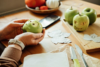 Halloween diy fruit ideas. female hands cutting out halloween green apple with creepy carved face