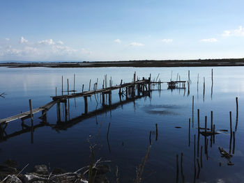 Wooden posts in lake against sky