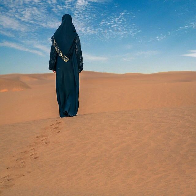 REAR VIEW OF A MAN STANDING ON SAND DUNE