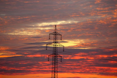 Low angle view of silhouette electricity pylon against orange sky