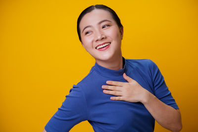 Portrait of smiling young woman against yellow background