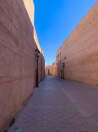 Footpath amidst buildings against blue sky
