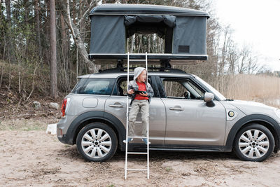 Boy standing on the ladder of a roof top tent whilst playing