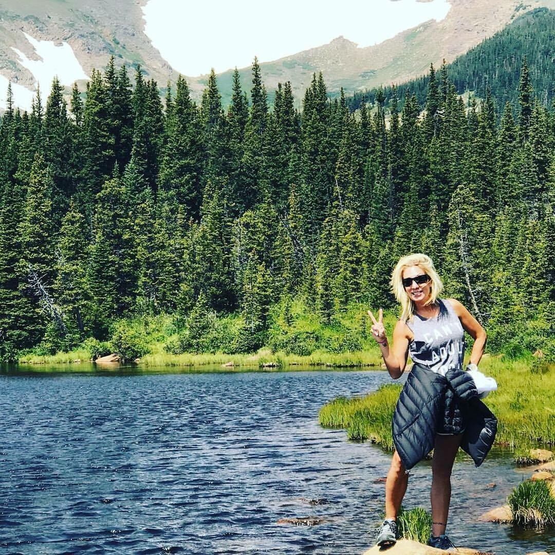 PORTRAIT OF SMILING YOUNG WOMAN STANDING BY RIVER AGAINST TREES