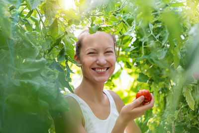 Portrait of young woman holding tomato amidst plant