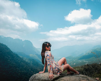 Woman sitting on mountain against sky