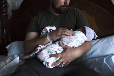 Cropped image of father carrying daughter while sitting on bed at home