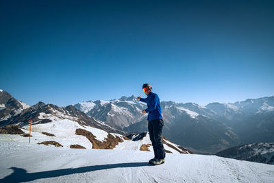 Rear view of man skiing on snowcapped mountain against clear blue sky